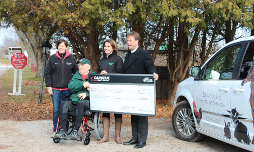 Collin Welsh of CARSTAR (right) hands over a donation cheque to representatives of WindReach Farms. CARSTAR has teamed with Enterprise Rent-A-Car to pay for the lease, insurance, maintenance and gas used in the Chrysler Town and Country seen here.